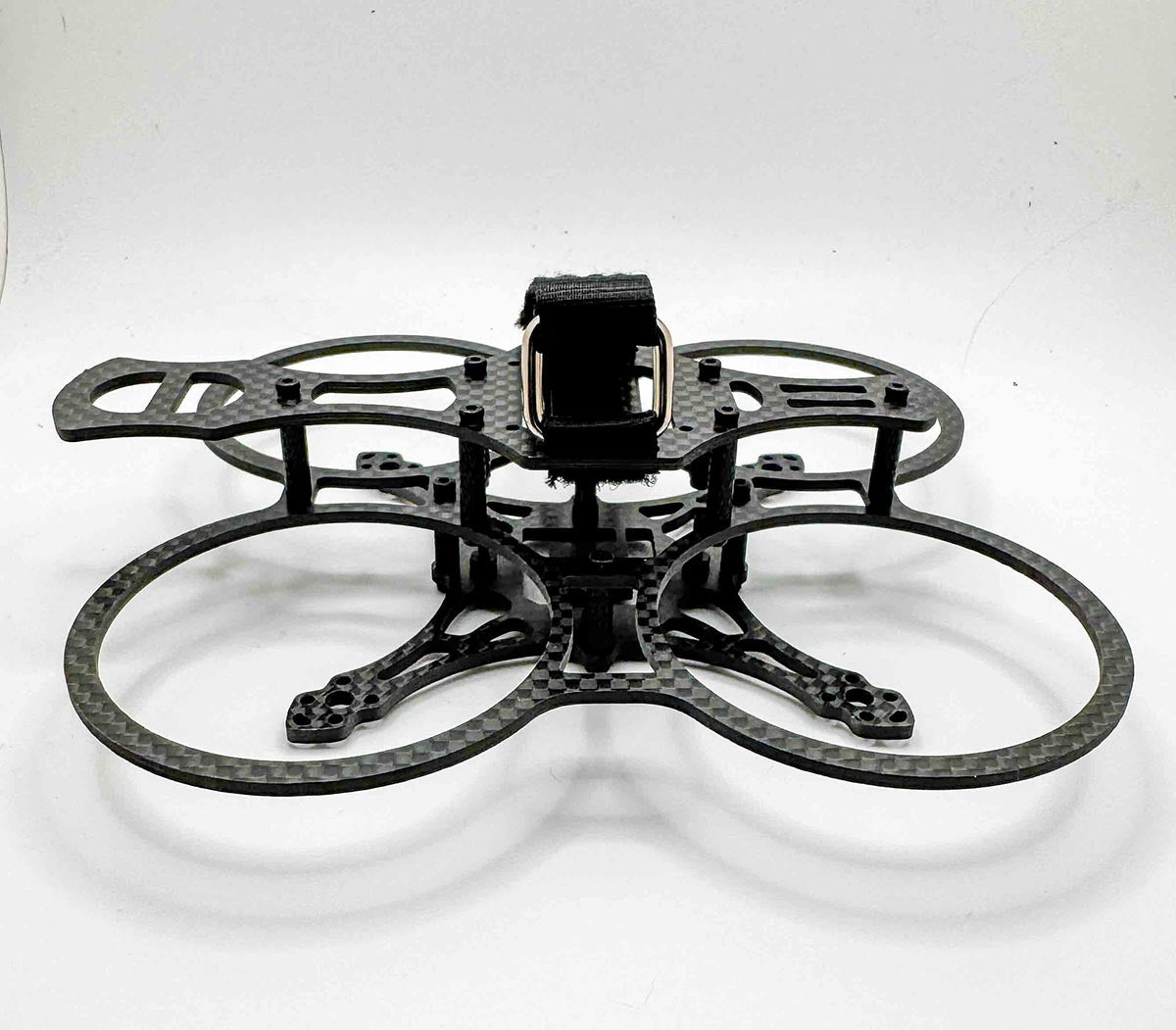 Side view of the Osito carbon fiber FPV drone frame with integrated prop guards and top-mounted battery strap; a durable micro frame inspired by both cinewhoops and freestyle rigs like the Pavo 20 Pro and AOS 2.0.